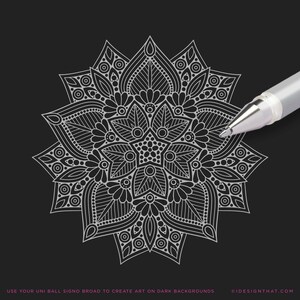 May include: A symmetrical mandala design in white ink on a black background. A silver pen is positioned near the mandala, suggesting the creation of art. The text at the bottom reads: USE YOUR UNI BALL SIGNO BROAD TO CREATE ART ON DARK BACKGROUNDS.