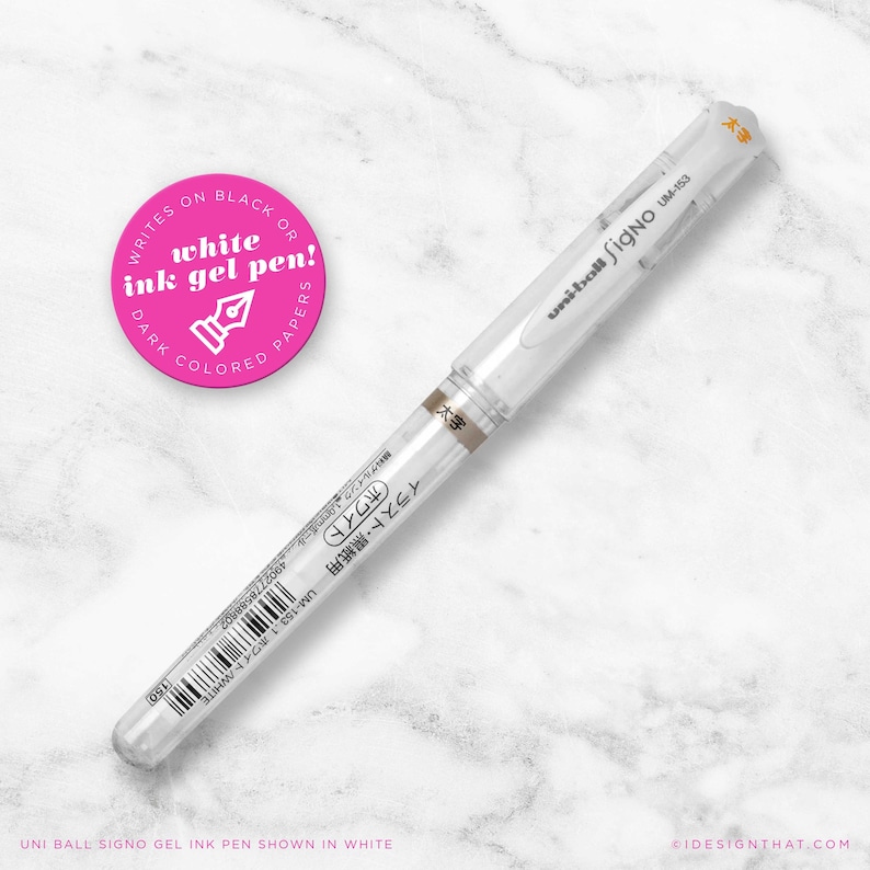 May include: A white Uni-ball Signo UM-153 gel ink pen on a marble surface. The pen has a clear barrel and a white ink cartridge. A pink circular sticker with the text "Writes on Black or Dark Coloured Papers" and "white ink gel pen!" is also visible.