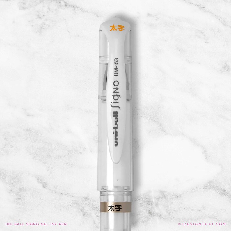 May include: A clear Uni-ball Signo gel ink pen with white accents and orange text. The pen has the text "uni-ball Signo UM-153" printed on the side. The pen also has the Japanese characters "太字" printed on the top and bottom.