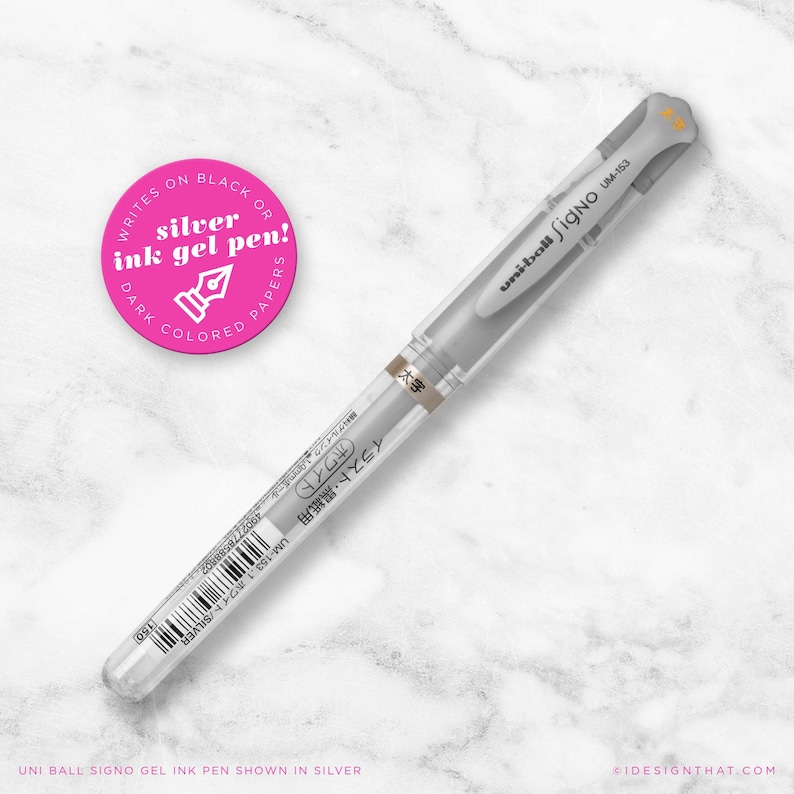 May include: A silver Uni-ball Signo UM-153 gel ink pen on a white marble surface. The pen has a clear barrel and a grey cap. A pink circular sticker with white text reads "Writes on Black or Dark Coloured Papers".