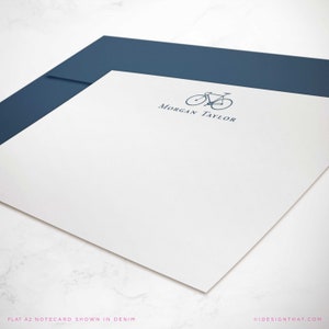 May include: A white A2 notecard with a blue bicycle logo and the text "Morgan Taylor" printed in blue ink. The notecard is shown with a blue envelope.