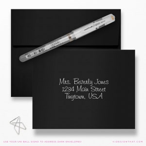May include: Black envelope and card with a white pen. The card displays a handwritten address in white ink: Mrs. Beverly Jones, 1234 Main Street, Tinytown, USA. The text at the bottom says: USE YOUR UNI BALL SIGNO TO ADDRESS DARK ENVELOPES!