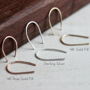 Pu&ograve; includere: Quattro stili diversi di orecchini a cerchio, ognuno con una finitura diversa: 14K Rose Gold Fill, Sterling Silver, 14K Gold Fill. Gli orecchini sono disposti in fila su una superficie di legno.