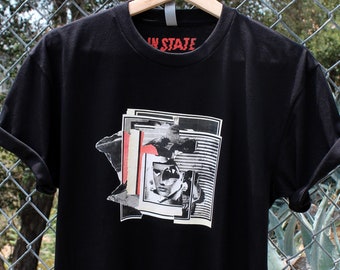 May include: Black t-shirt with a graphic print of a person's face in a collage style. The text "In State" is printed on the neck of the shirt.