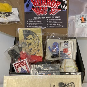 May include: A black box filled with various magic tricks, including a ghost clock, a zombie with a brain, a floating shrunken head, a monkey's paw, a Hercules death pillar, a phantom dollar bill, a spirit time, a mind reading Swami, a deep space terror, a haunted severed finger, and a deck of Maverick playing cards.
