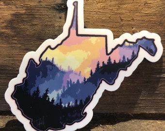 May include: A sticker of the state of West Virginia with a silhouette of a forest and a sunset in the background. The sticker is white with a purple, pink, yellow, and blue design.