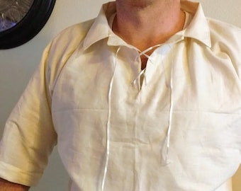 May include: A white short-sleeved shirt with a lace-up neckline and a white collar. The shirt is tucked into dark blue pants with two brown buttons on the waistband.