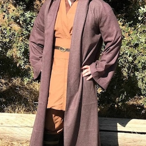 May include: A person wearing a brown hooded robe with a brown belt and a brown undershirt. The robe has a long, flowing design and is made of a soft, comfortable fabric.