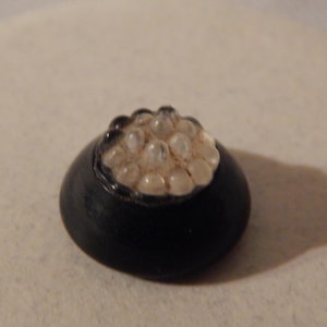 May include: A small black bowl filled with white pearl-like beads.