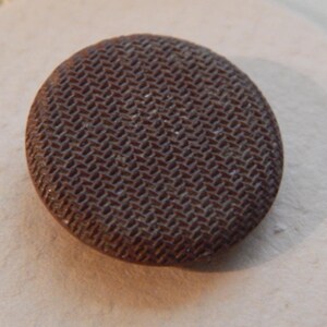 Könnte beinhalten: Ein brauner Knopf mit einer strukturierten Oberfläche. Der Knopf ist rund und hat einen Durchmesser von etwa 2,5 cm.