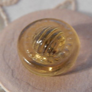 May include: A clear glass button with a raised, textured, yellow center. The button is round and has a smooth, polished surface.