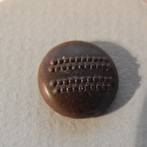 Może przedstawiać: Brązowy guzik z dwoma rzędami wypukłych kropek.