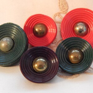 Puede incluir: Cuatro botones decorativos con un diseño de círculos concéntricos. Los botones son rojos, verdes y morados con centros dorados.