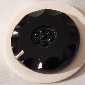 May include: Black glass button with a scalloped edge and a central design of eight smaller circles.