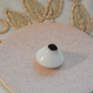 Può includere: Un occhio di vetro bianco con pupilla nera, utilizzato per la creazione di bambole o per l'artigianato.