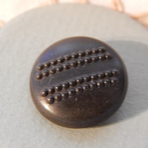 Può includere: Un bottone marrone scuro con due file di punti in rilievo attorno al bordo.