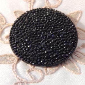 May include: A black round button with a textured surface that resembles tiny black beads.