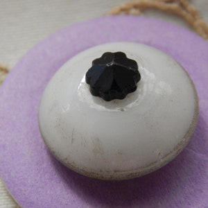 Può includere: Un bottone in ceramica bianca con un strass nero a forma di stella al centro.