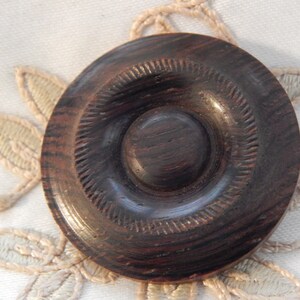 May include: A dark brown wooden button with a concentric circle design. The button has a smooth, polished finish.