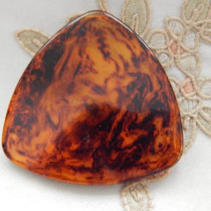 May include: A triangular, tortoiseshell-patterned object with a smooth, glossy surface. The colors range from dark brown to amber, creating a marbled effect. The object is likely a decorative item or accessory.