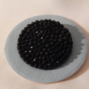 May include: A black button covered in small black beads, set on a light blue background.