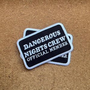 Może przedstawiać: Dwie czarne prostokątne naszywki z białym tekstem i obramowaniem. Tekst na naszywkach brzmi "DANGEROUS NIGHTS CREW OFFICIAL MEMBER". Naszywki są ułożone jedna na drugiej.