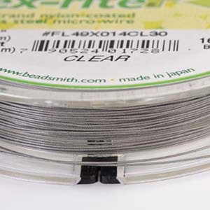 Peut inclure: Une bobine de fil micro en acier recouvert de nylon transparent pour la fabrication de bijoux. La bobine est étiquetée avec le numéro de produit #FL40X014CL30 et le mot CLEAR.