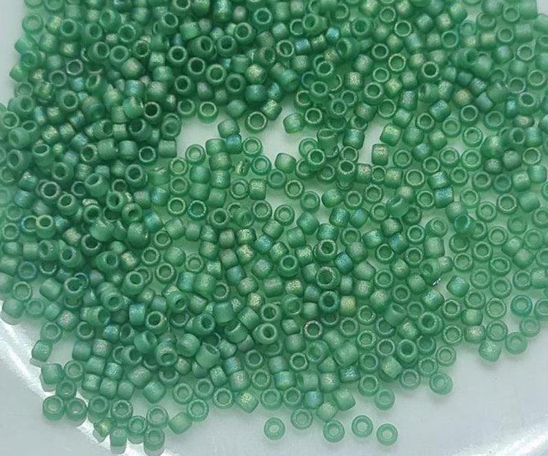 May include: A close-up view of a large quantity of small, round, green glass beads. The beads have a slightly iridescent finish.