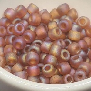 Pode incluir: Um monte de pequenas contas de vidro redondas e iridescentes de cor rosa claro. As contas t&ecirc;m um brilho ligeiramente met&aacute;lico e s&atilde;o perfeitas para a fabrica&ccedil;&atilde;o de joias.