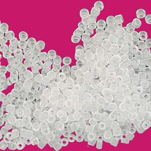 May include: A large pile of clear plastic beads. The beads are small and round, and they are scattered randomly on a pink background.