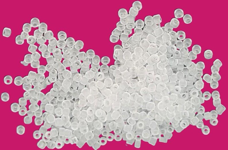 May include: A large pile of clear plastic beads. The beads are small and round, and they are scattered randomly on a pink background.