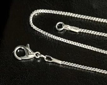 May include: A silver chain necklace with a lobster clasp closure. The chain is made of small, linked squares.