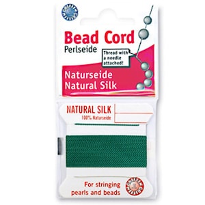 Op de afbeelding: Een verpakking met groene kralenkoord van natuurzijde. De verpakking bevat de tekst "Bead Cord", "Natural Silk" en "For stringing pearls and beads". Het pakket bevat ook een draad met een naald.