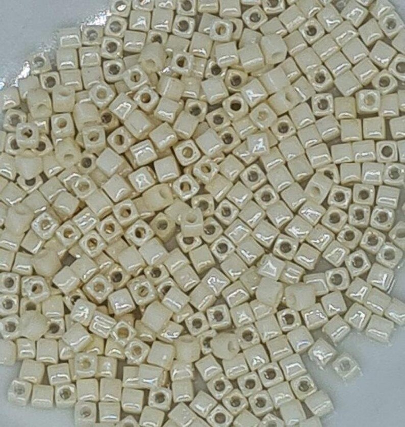 Puede incluir: Una gran cantidad de peque&ntilde;as cuentas cuadradas de color blanco roto con un ligero brillo iridiscente.