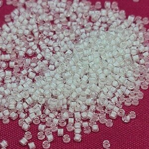 May include: A large pile of small, clear, iridescent glass beads. The beads are round and have a slightly flattened shape. They are arranged in a random pattern.