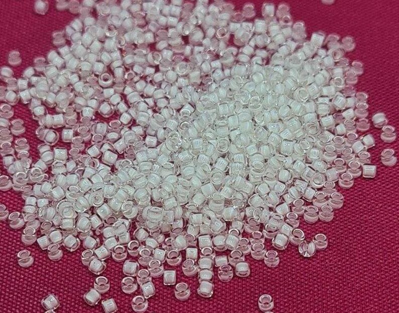 May include: A large pile of small, clear, iridescent glass beads. The beads are round and have a slightly flattened shape. They are arranged in a random pattern.