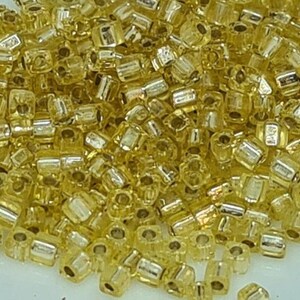 Puede incluir: Un mont&oacute;n grande de peque&ntilde;as cuentas de vidrio de color dorado. Las cuentas son redondas y tienen un acabado brillante y met&aacute;lico.