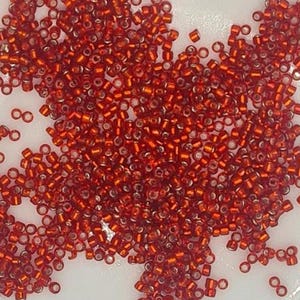 May include: A large pile of small, red, glass seed beads. The beads are translucent and have a slight shimmer.