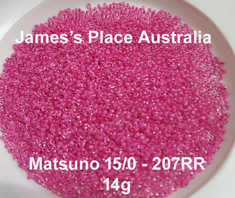 May include: A close-up of a large quantity of pink seed beads. The beads are in a white bowl and the text "James's Place Australia" and "Matsuno 15/0 - 207RR 14g" is visible.
