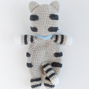 May include: A crocheted gray and black striped cat toy with a blue collar. The cat has a white belly and a white tip on its tail.