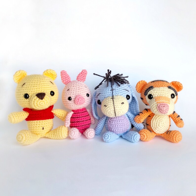May include: Four crocheted stuffed animal characters: Winnie the Pooh, Piglet, Eeyore, and Tigger. The characters are all smiling and have embroidered features.