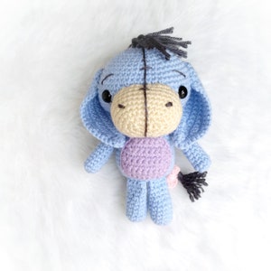 May include: A crocheted stuffed animal toy resembling a donkey. The toy is blue with a purple belly and a black tail. It has black eyes and a beige nose.