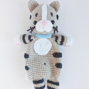 May include: A crocheted stuffed cat toy with gray and white stripes, black spots, and a light blue collar. The cat is lying on its back with its paws in the air.