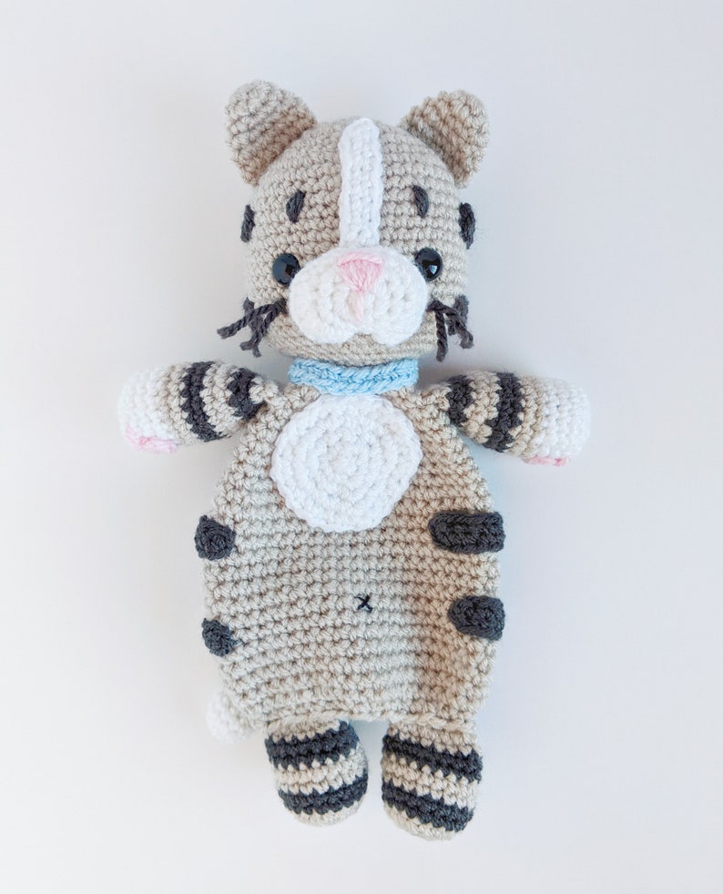 May include: A crocheted stuffed cat toy with gray and white stripes, black spots, and a light blue collar. The cat is lying on its back with its paws in the air.