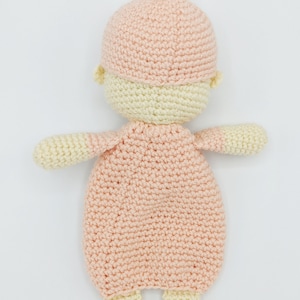 May include: A crocheted baby doll with a pink hat and a pink and cream outfit. The doll is lying on its back with its arms outstretched.