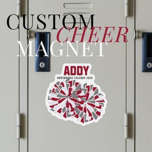 May include: A custom cheer magnet with the name "Addy" and "Northridge Falcons 2025" printed on it. The magnet features a pom-pom design in red, white, and gray colors. The words "Custom Cheer Magnet" are printed above the magnet.