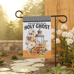 May include: A rectangular garden flag featuring a black and white striped top border and an orange bottom section. The text reads THERE IS NO GHOST LIKE THE HOLY GHOST and HAPPY FALL. A ghost holds a book next to a lantern and a pumpkin with flowers.
