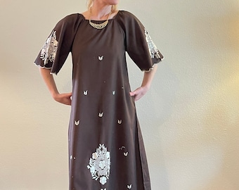 May include: A brown maxi dress with white floral embroidery. The dress features short sleeves with scalloped edges and a scoop neckline. White floral designs are embroidered on the sleeves and the lower portion of the dress.