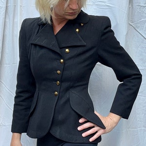 May include: A black fitted blazer with a pointed collar and gold buttons. The blazer has a cinched waist and a peplum hem.