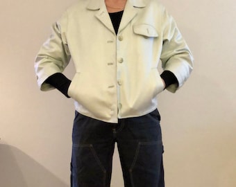 May include: A light green satin jacket with a button-up front and two pockets. The jacket has a cropped length and a relaxed fit.